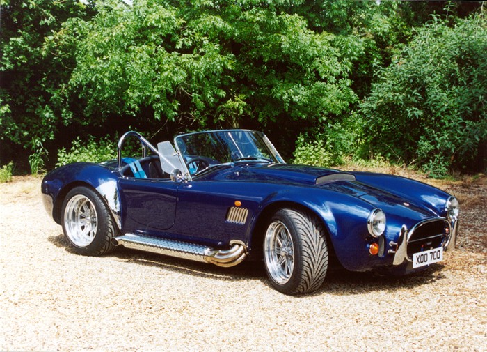 Finished blue AK427 Cobra parked in front of green hedges